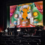 Promo image showing Andrew Earle Simpson conducting a chamber ensemble in front of a screen showing Disney's Music Land