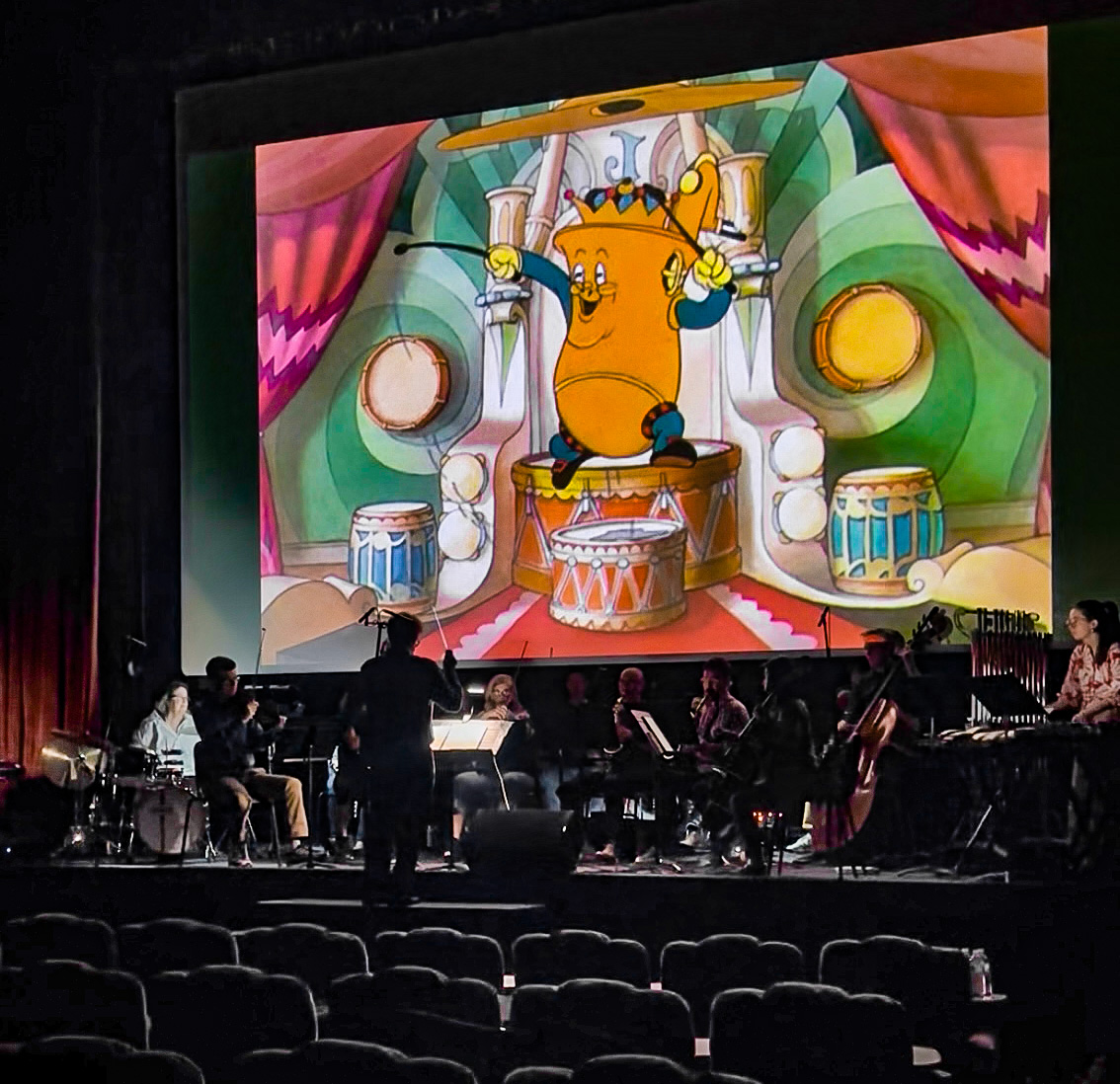 Promo image showing Andrew Earle Simpson conducting a chamber ensemble in front of a screen showing Disney's Music Land